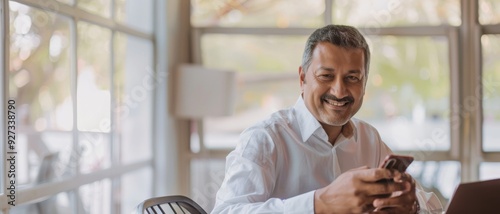 A middle-aged man in an office setting, smiling engagingly as he looks at his smartphone, capturing a moment of connection and modern interaction. photo