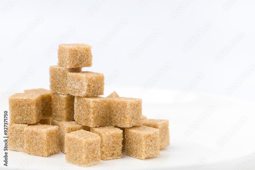 Brown sugar cubes on white plate on white background. Selective focus. Brown sugar cubes on white plate on white background. Selective focus.