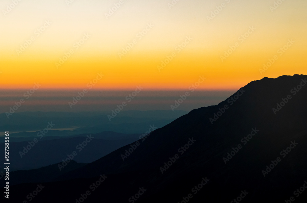 Sunrise over mountain silhouettes with a vibrant gradient sky transitioning from dark orange to pale yellow, creating a serene and tranquil atmosphere Sunrise over mountain silhouettes with a vibrant gradient sky transitioning from dark orange to pale yellow, creating a serene and tranquil atmosphere