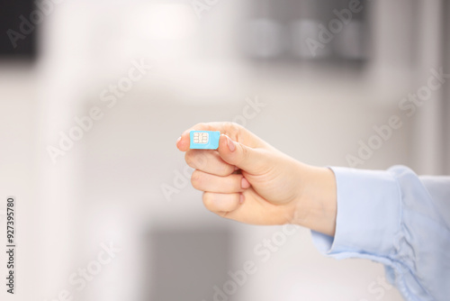 Woman holding SIM card indoors, closeup. Space for text