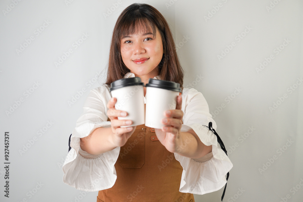 Excited young asian woman wearing long white sleeve shirt and brown apron is holding and serving coffee drinks to customer with smiling face expression. Isolated over white background. Excited young asian woman wearing long white sleeve shirt and brown apron is holding and serving coffee drinks to customer with smiling face expression. Isolated over white background.