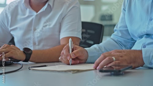 Close up of businessman's hands in company meeting taking notes with pen on paper during daytime
