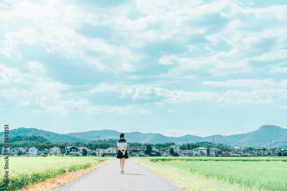 夏の田んぼ道を歩いていく三つ編みのセーラ服の女の子 夏の田んぼ道を歩いていく三つ編みのセーラ服の女の子