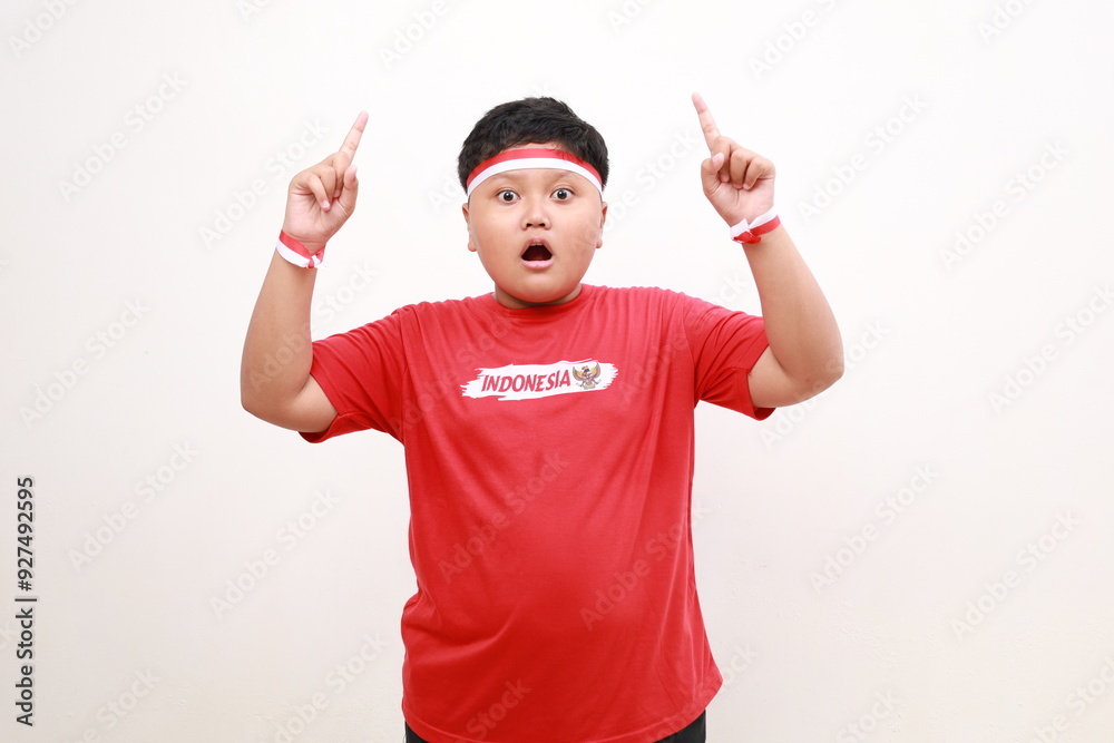 Wow shocked Asian boy wearing Indonesia flag colored headband and casual outfit while smiling cheerfully and pointing above at the copy space. Independence day advertisement concept Wow shocked Asian boy wearing Indonesia flag colored headband and casual outfit while smiling cheerfully and pointing above at the copy space. Independence day advertisement concept