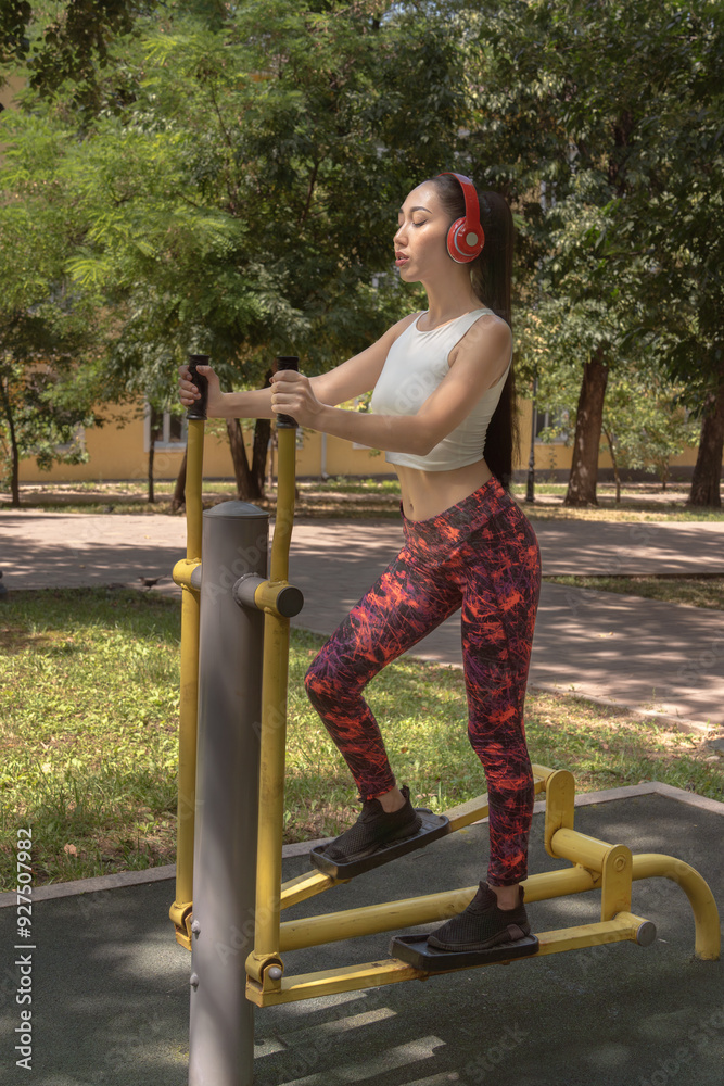 Fototapeta premium Beautiful Asian girl doing sports on the trainer in the park. Fitness. Healthy lifestyle