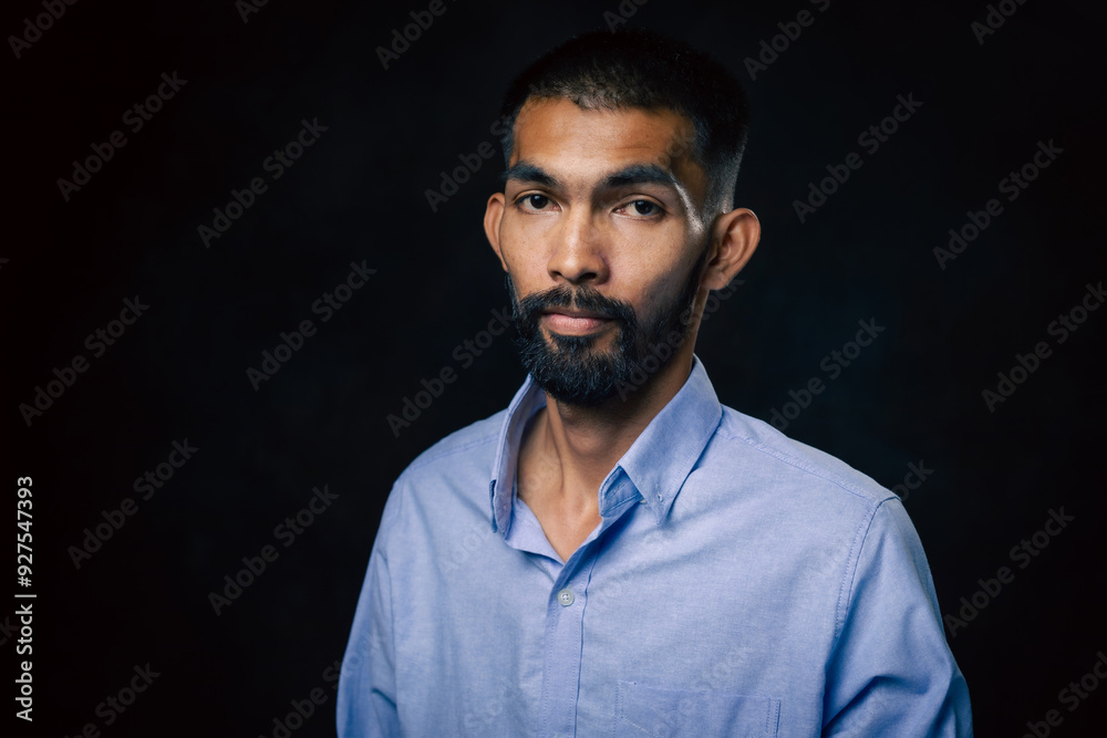 Obraz premium Portrait of bearded handsome Asian man in a pensive mood and looking at camera in black studio background.