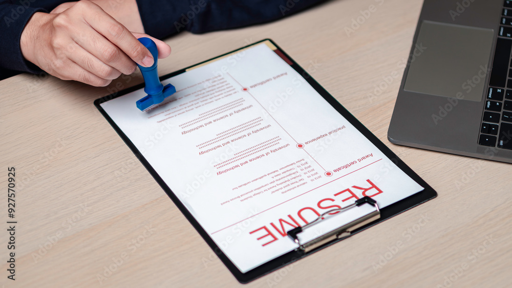 a person stamping a resume. suggesting an approval or verification action. a recruitment or human resources context, where resumes are reviewed and approved for further consideration