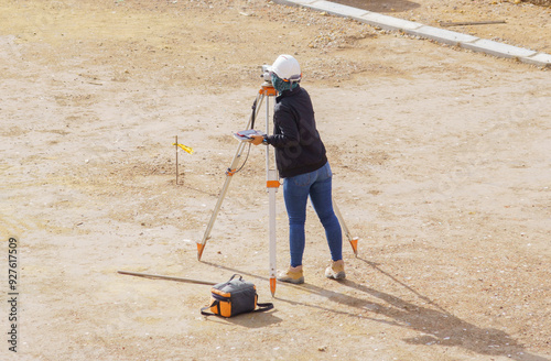 A woman is at a construction site with a topographic device performing terrain analysis.