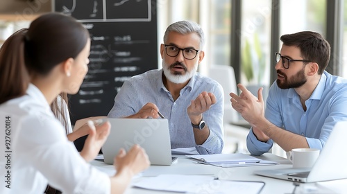 A diverse group of professionals discuss ideas in a modern office setting. A middle-aged Caucasian man is engaged in conversation with two colleagues.
