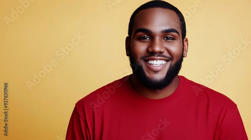 A smiling African American man in a red shirt poses against a bright yellow background, exuding warmth and positivity, showcasing his well-groomed beard and joyful demeanor.