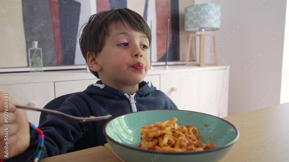 Child twirling spaghetti with a fork, gripping it tightly while intensely focused on the meal, highlighting the effort and engagement in self-feeding within a familiar home environment Child twirling spaghetti with a fork, gripping it tightly while intensely focused on the meal, highlighting the effort and engagement in self-feeding within a familiar home environment