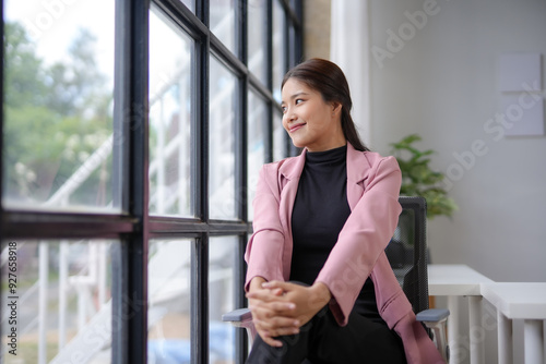 Young asian businesswoman is sitting in her office, smiling and looking out the window, enjoying a moment of peace Free Download Young asian businesswoman is sitting in her office, smiling and looking out the window, enjoying a moment of peace - GFXLoad