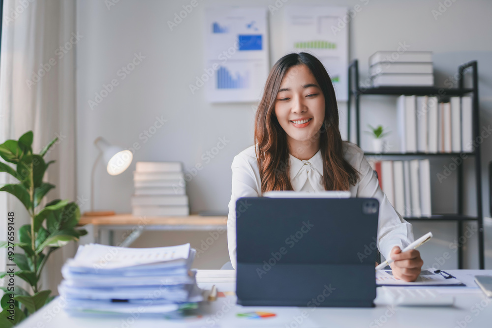 Asian businesswoman is smiling while working from her home office using a digital tablet Asian businesswoman is smiling while working from her home office using a digital tablet