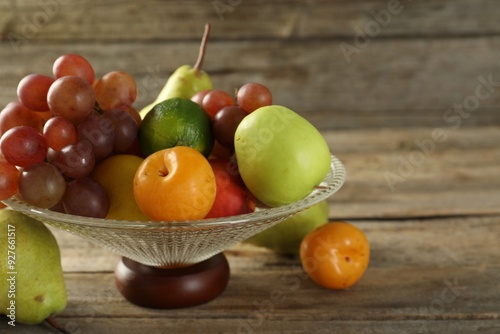 Glass vase with different fresh fruits on wooden table, closeup