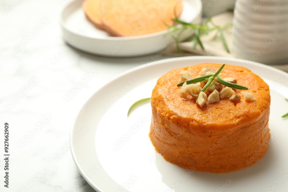 Plate with tasty mashed sweet potato, rosemary and walnuts on white table, closeup