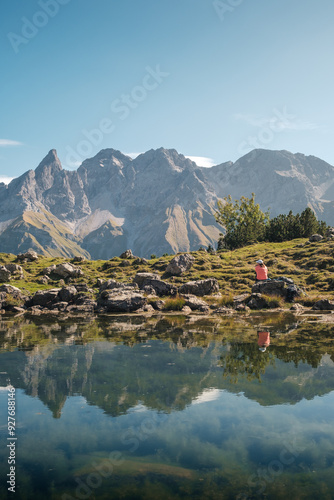 View of a mountain lake in Germany with a seated hiker on the shore. In the background the mountain Trettachspitze and Mädelegabel near Oberstdorf. photo