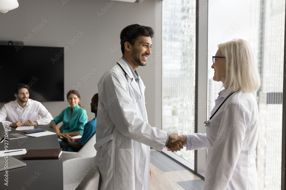 © fizkes - Two friendly smiling multiethnic therapists colleagues shaking hands standing in conference room, greeting each other, lead pleasant friendly talk after medical council meeting in clinic boardroom © fizkes - Two friendly smiling multiethnic therapists colleagues shaking hands standing in conference room, greeting each other, lead pleasant friendly talk after medical council meeting in clinic boardroom