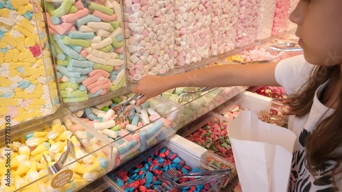 Little girl daughter picking up sweet candies in a candy shop with colorful interior