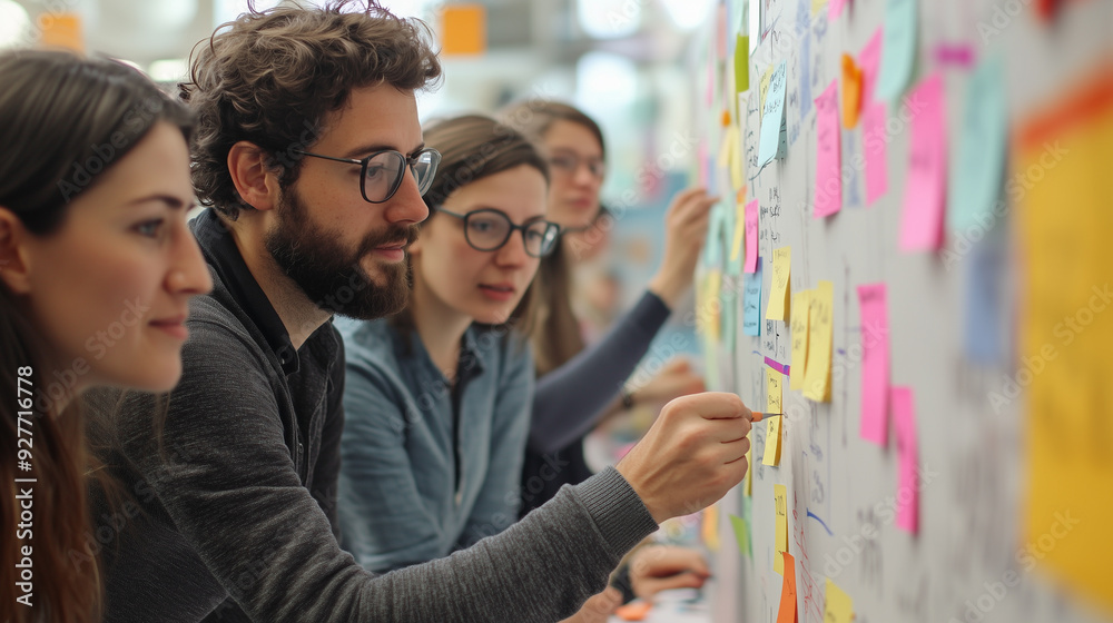 Young entrepreneurs collaborate and generate new concepts using colorful sticky notes on a whiteboard during a brainstorming session