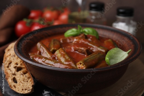 Tasty stew with okra, tomato sauce, bread and basil on wooden table, closeup