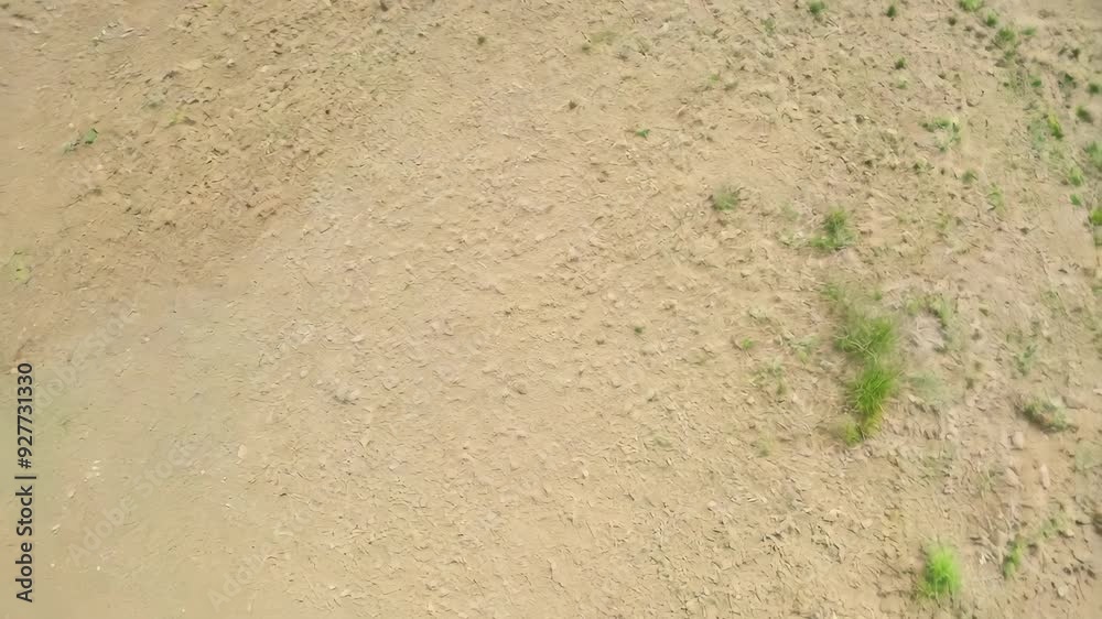 Rotating top view of dry sand with sparse grass patches, creating a minimalistic and natural texture across the entire frame