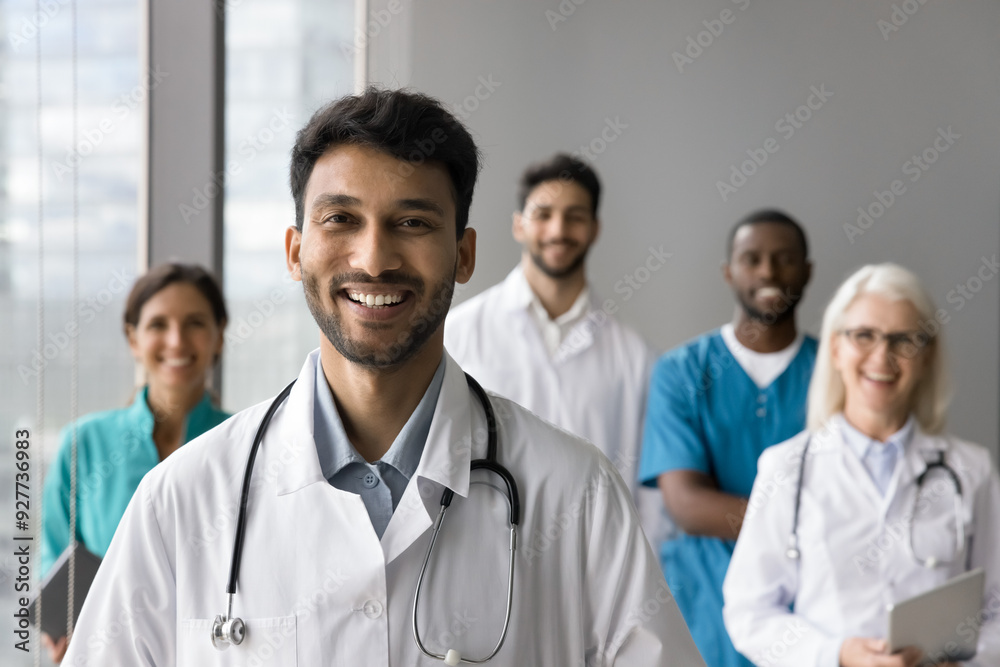 Head shot portrait of smiling Indian male general practitioner, surgeon or cardiologist, medical worker wear white coat posing with clinic staff. Medicine, insurance, professional healthcare services Head shot portrait of smiling Indian male general practitioner, surgeon or cardiologist, medical worker wear white coat posing with clinic staff. Medicine, insurance, professional healthcare services