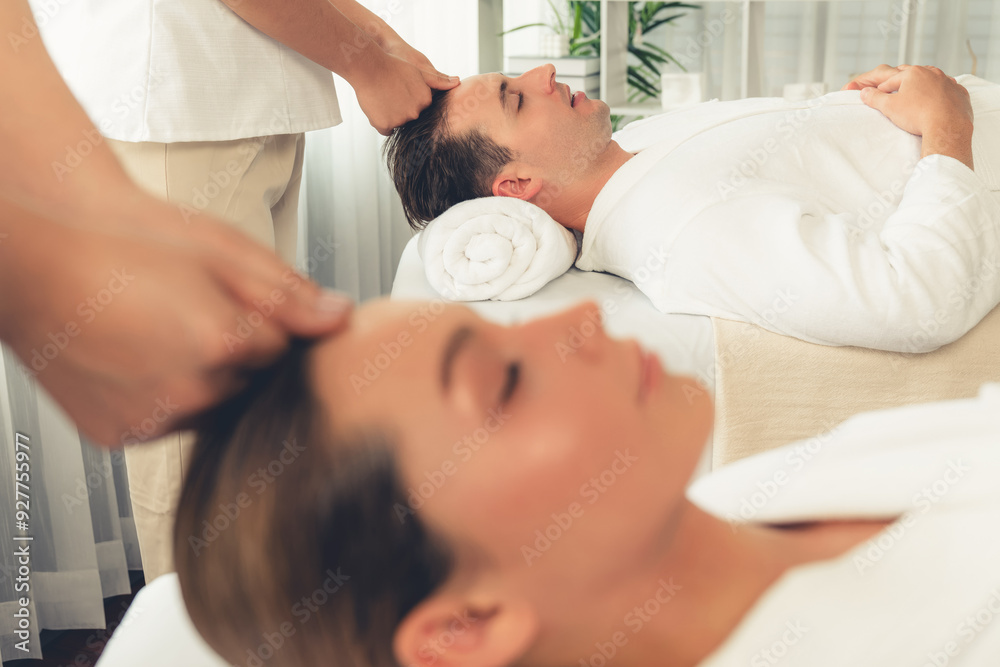 Caucasian couple enjoying relaxing anti-stress head massage and pampering facial beauty skin recreation leisure in dayspa modern light ambient at luxury resort or hotel spa salon. Quiescent