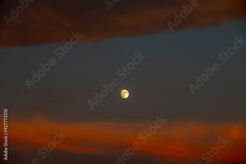 Full moon between orange clouds at dusk