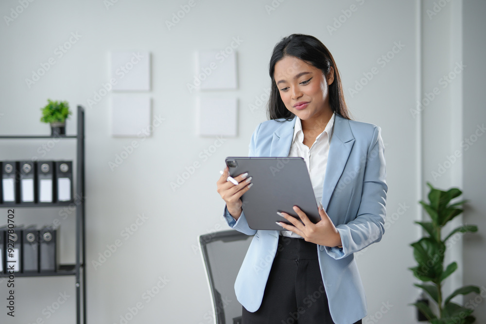 Young manager woman is standing in her office, holding a tablet and looking at the screen Young manager woman is standing in her office, holding a tablet and looking at the screen