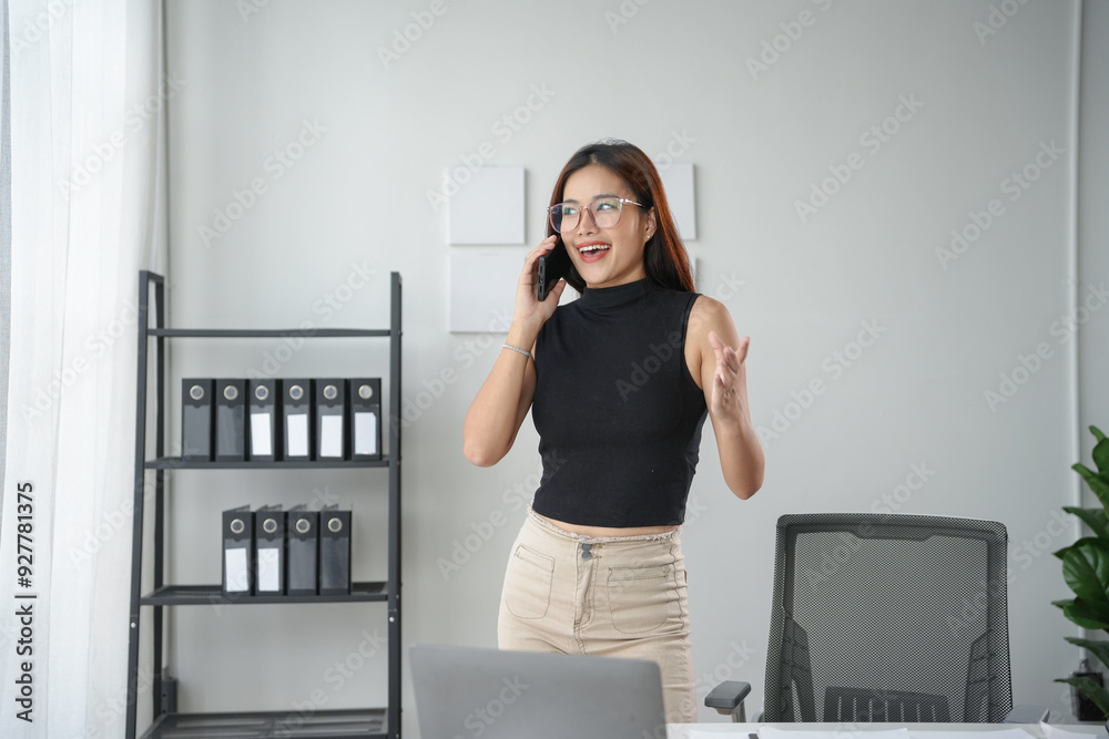 Young manager is standing in her office, talking on the phone and gesturing with one hand Young manager is standing in her office, talking on the phone and gesturing with one hand