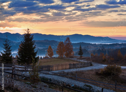 Early morning misty autumn slopes of Carpathian Mountains and rural road in mountain village (Yablunytsia village and pass, Ivano-Frankivsk oblast, Ukraine). Goverla and Petros mountains in far. photo