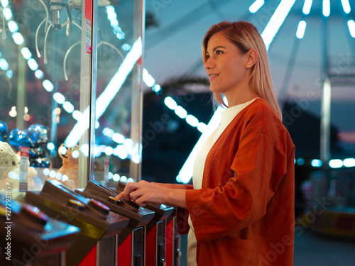 Girl plaing claw machine on a fun fair amusiment park. Night fair illumination, Ferris wheel spinning in the background