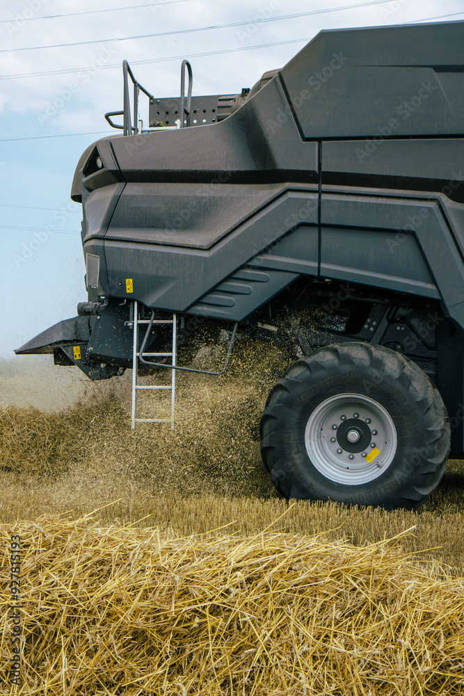 Side view of a combine harvester in a wheat field, focusing on the machinery's tire and chaff dispersion. Advanced farming technology during harvest season. Agricultural efficiency. Vertical photo