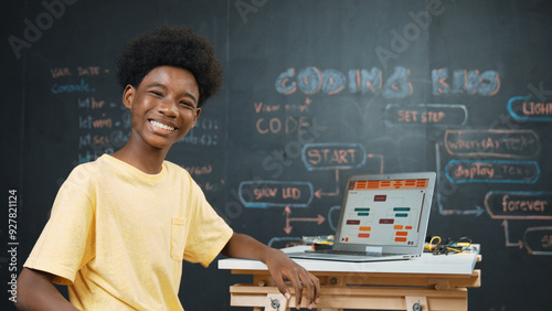 African boy using laptop programing system or coding prompt and turn around to smile to camera. Highschool student working learning to write engineering code while sitting blackboard. Edification.