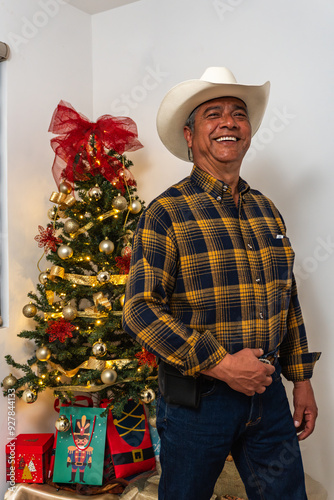 Smiling Mexican Man in Cowboy Hat Posing by Christmas Tree with Festive Gifts