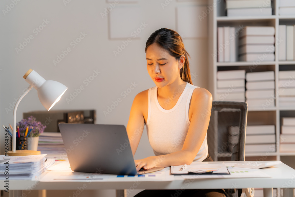 A determined young woman analyzes data on a clipboard while working late at her desk. It is illuminated by a table lamp. This image evokes a feeling of dedication and perseverance. A determined young woman analyzes data on a clipboard while working late at her desk. It is illuminated by a table lamp. This image evokes a feeling of dedication and perseverance.