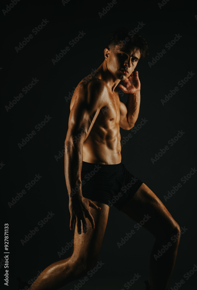 Obraz premium Muscular male athlete posing in a dark room showcasing strength, fitness, and a well-defined physique. Ideal image for health and fitness related content.