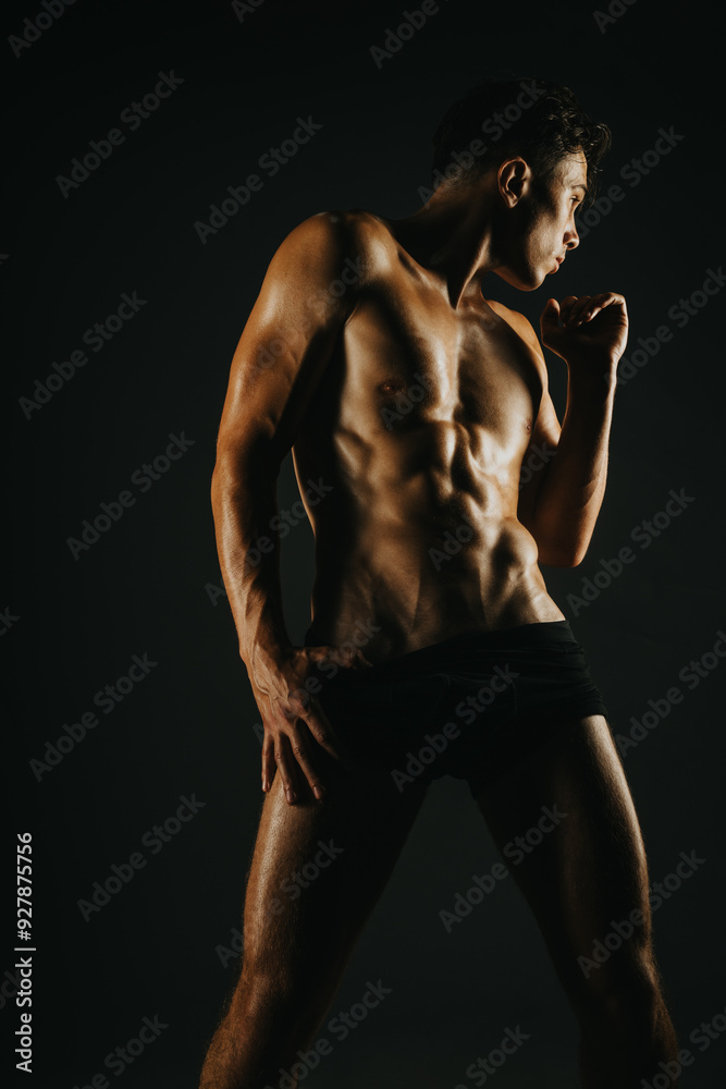 Muscular man striking a pose in a dark studio setting, with dramatic lighting highlighting his well-defined abs and muscular build. Muscular man striking a pose in a dark studio setting, with dramatic lighting highlighting his well-defined abs and muscular build.