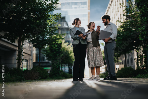 Business colleagues enjoying a friendly conversation outside an office building surrounded by greenery on a sunny day.