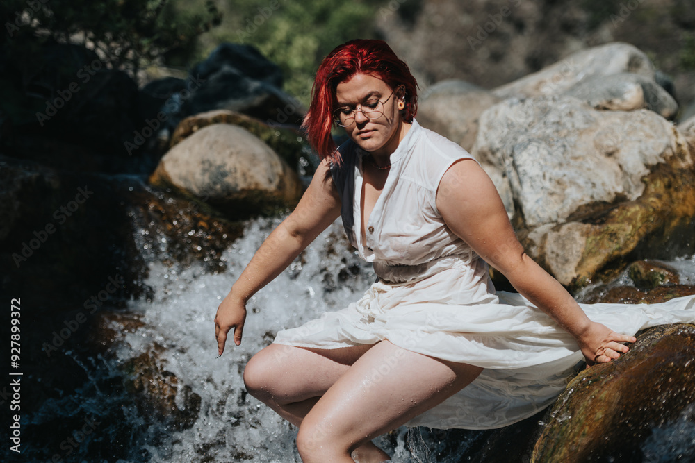 Woman in a white dress with red hair sitting by a rocky waterfall enjoying the peaceful natural surroundings. Woman in a white dress with red hair sitting by a rocky waterfall enjoying the peaceful natural surroundings.