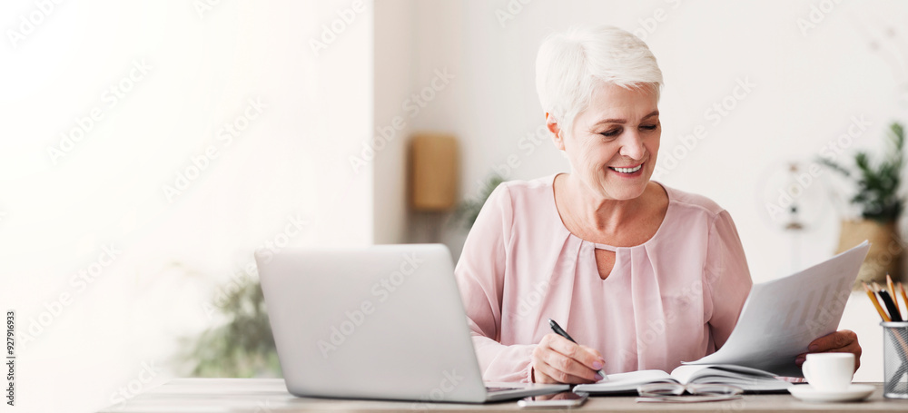 Mature editor reading printed text, making notes, using laptop, working from home, copy space Mature editor reading printed text, making notes, using laptop, working from home, copy space