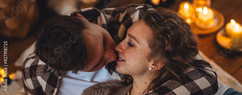 Beautiful young loving couple relaxing near fireplace in bed at home. Happy spouses enjoying lazy romantic winter cozy morning in bedroom. Candles, garlands, countryside interior. Romantic date banner