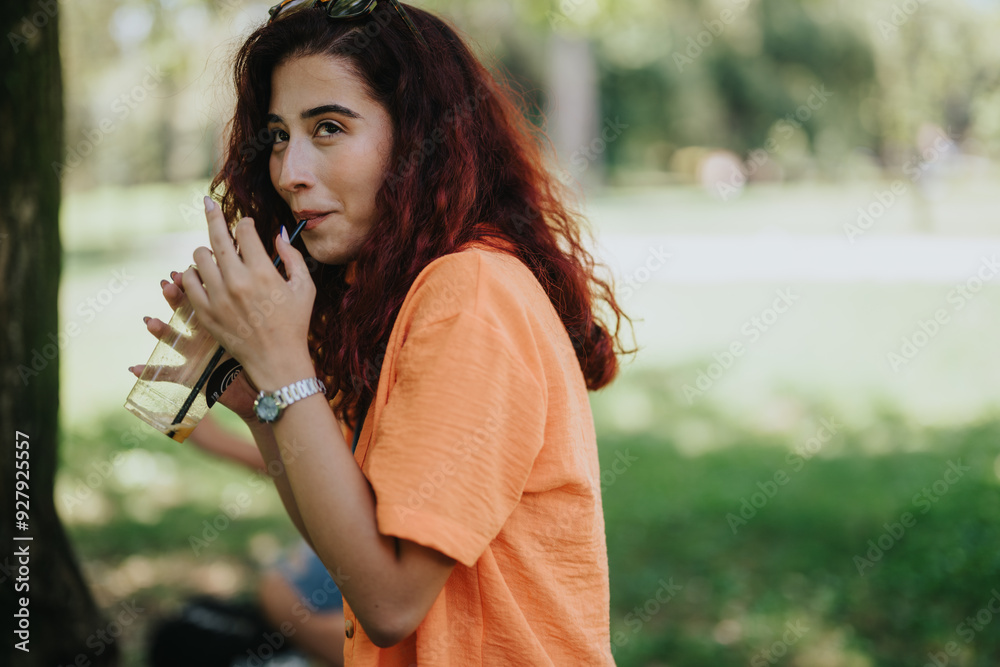 Young woman enjoying a refreshing drink in the park on a sunny day, relaxing and having a good time outdoors. Young woman enjoying a refreshing drink in the park on a sunny day, relaxing and having a good time outdoors.