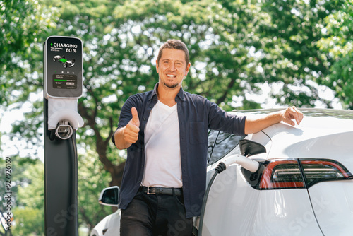 Man recharging battery for electric car during road trip travel EV car in natural forest or national park. Eco friendly travel during vacation and holiday. Exalt