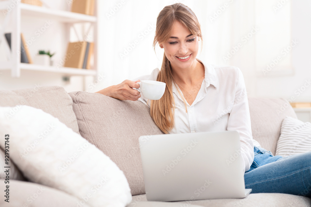 Cheerful Woman Using Laptop Having Coffee On Weekend Morning Sitting On Sofa At Home. Selective Focus Cheerful Woman Using Laptop Having Coffee On Weekend Morning Sitting On Sofa At Home. Selective Focus