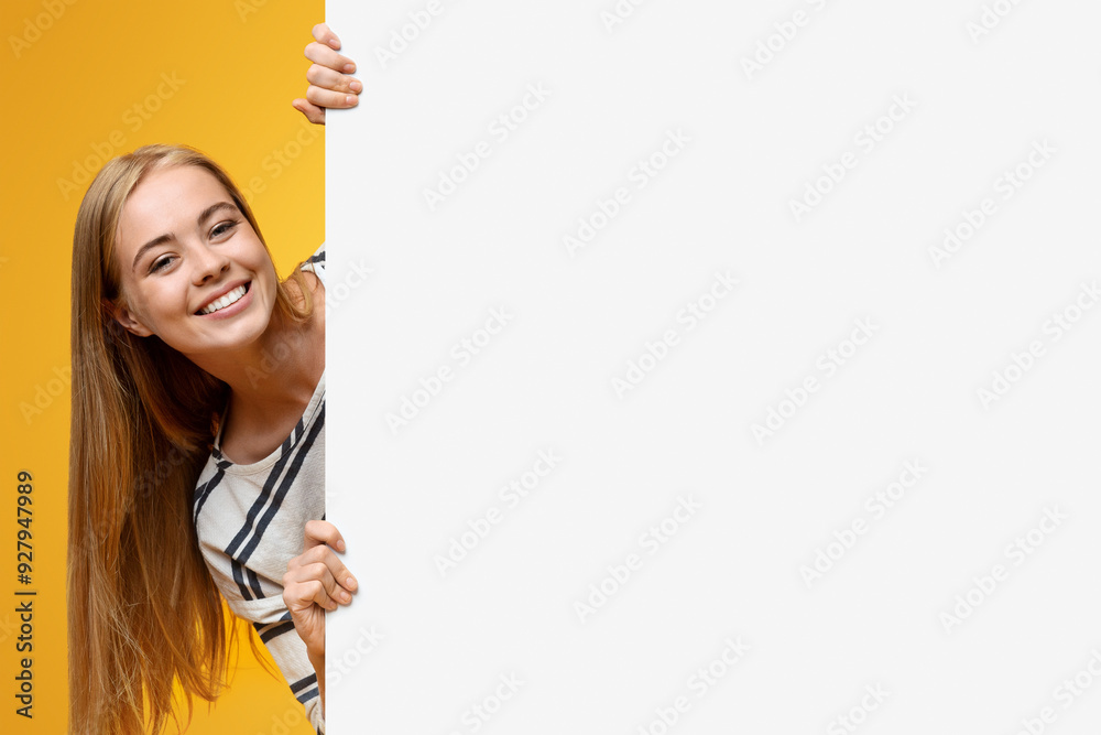 © Prostock-studio - Cute teenage girl looking out of white blank placard for your text or product, yellow background