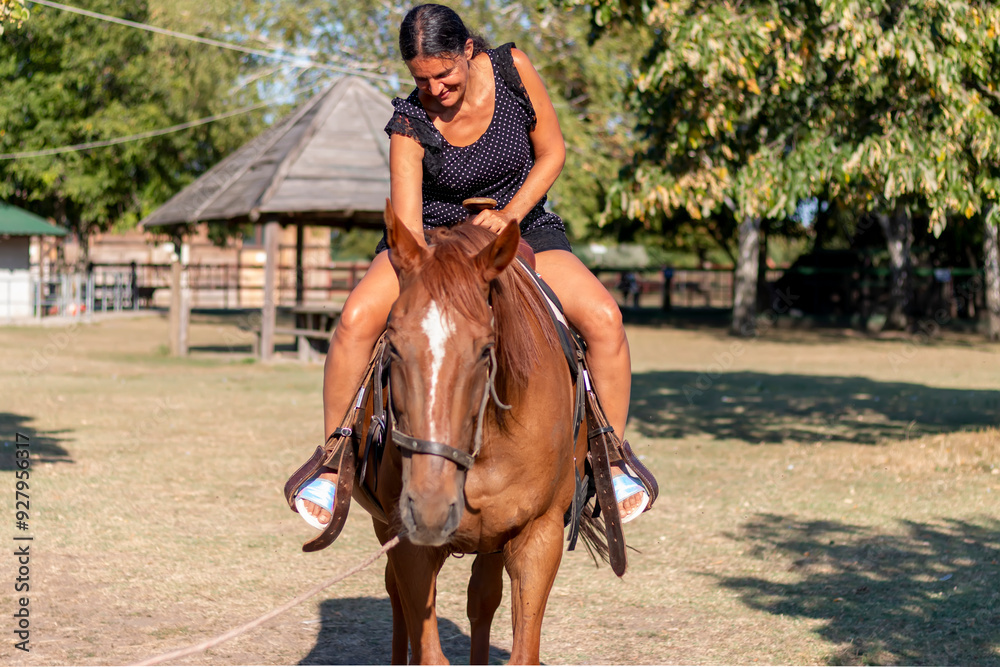 Happy middle-aged woman riding brown horse on the ranch Happy middle-aged woman riding brown horse on the ranch