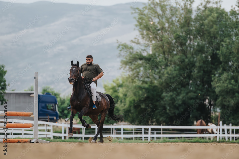 Man riding a horse during equestrian practice in an outdoor arena with a scenic mountain background. Man riding a horse during equestrian practice in an outdoor arena with a scenic mountain background.