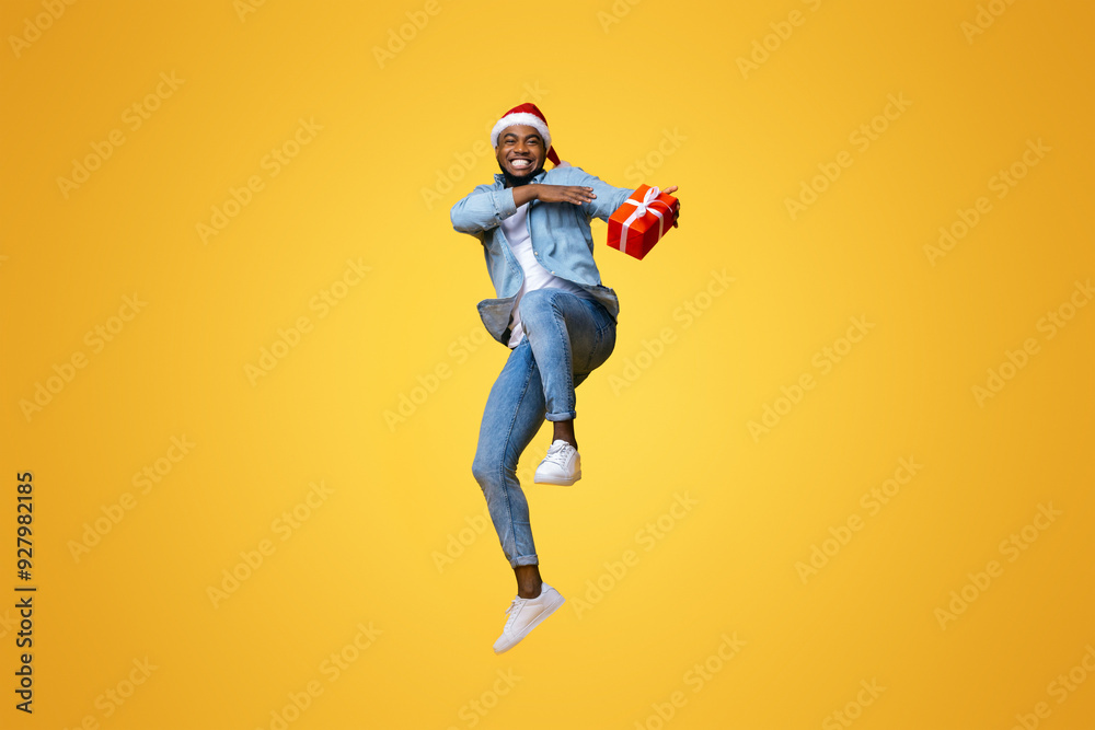 Christmas delivery concept. Positive african american guy jumping with Xmas present, hurry to deliver gift box in time. yellow background Christmas delivery concept. Positive african american guy jumping with Xmas present, hurry to deliver gift box in time. yellow background