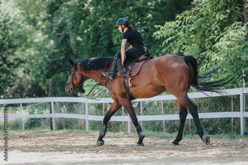 Woman enjoying horseback riding in an outdoor arena with lush green trees in the background. A tranquil moment of connection between rider and horse.